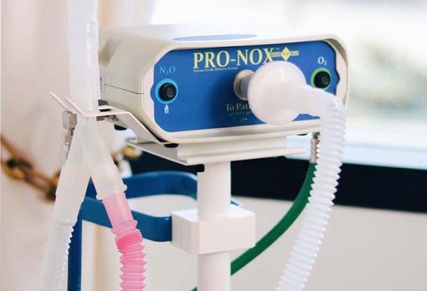 is-pro-nox-safe-img Close-up of a Pro-Nox nitrous oxide delivery system with a blue front panel and connected tubing on a stand in a clinical setting.