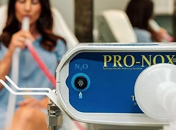 Close-up of a PRO-NOX nitrous oxide delivery machine in a clinic, with a patient in the background using a mask for sedation.