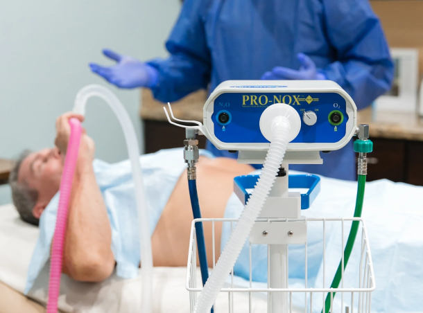 why-we-added-our-practice-img Anesthesia machine with tubes connected to a patient lying on a hospital bed during a procedure at a medical facility.